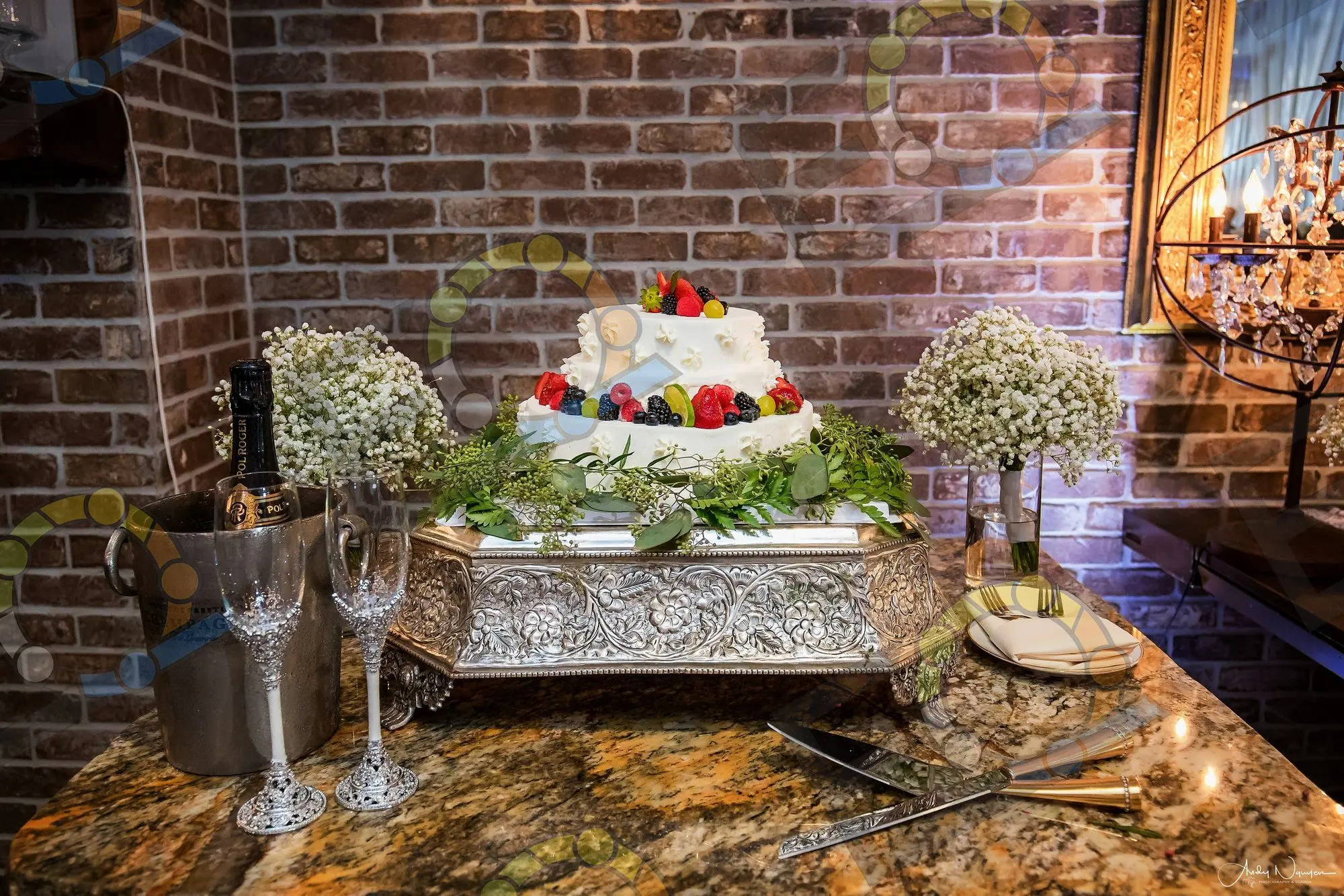 A berry-topped cake on a silver tray against a brick wall