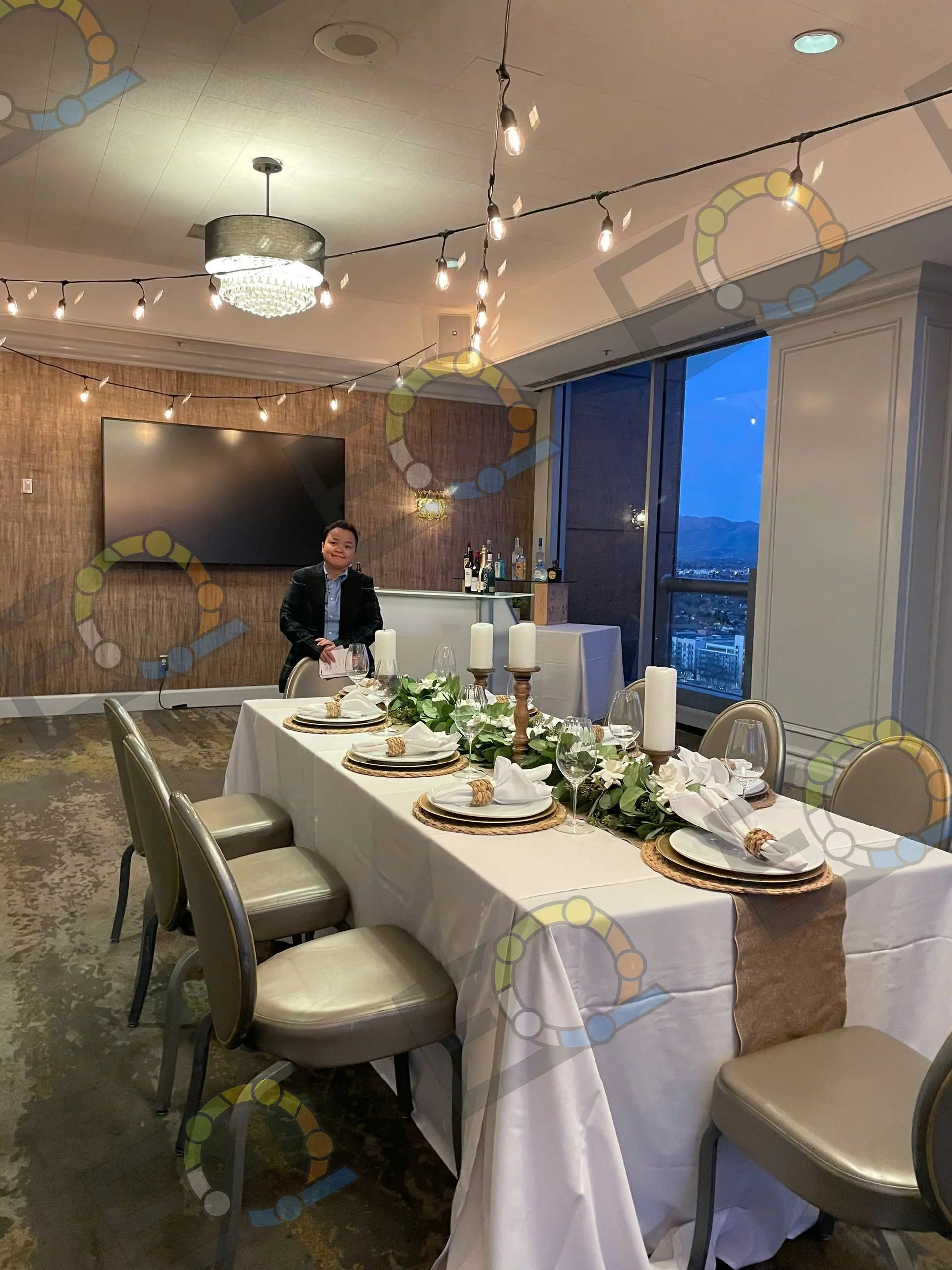 A long table set for dinner under track lighting, with the city through the window