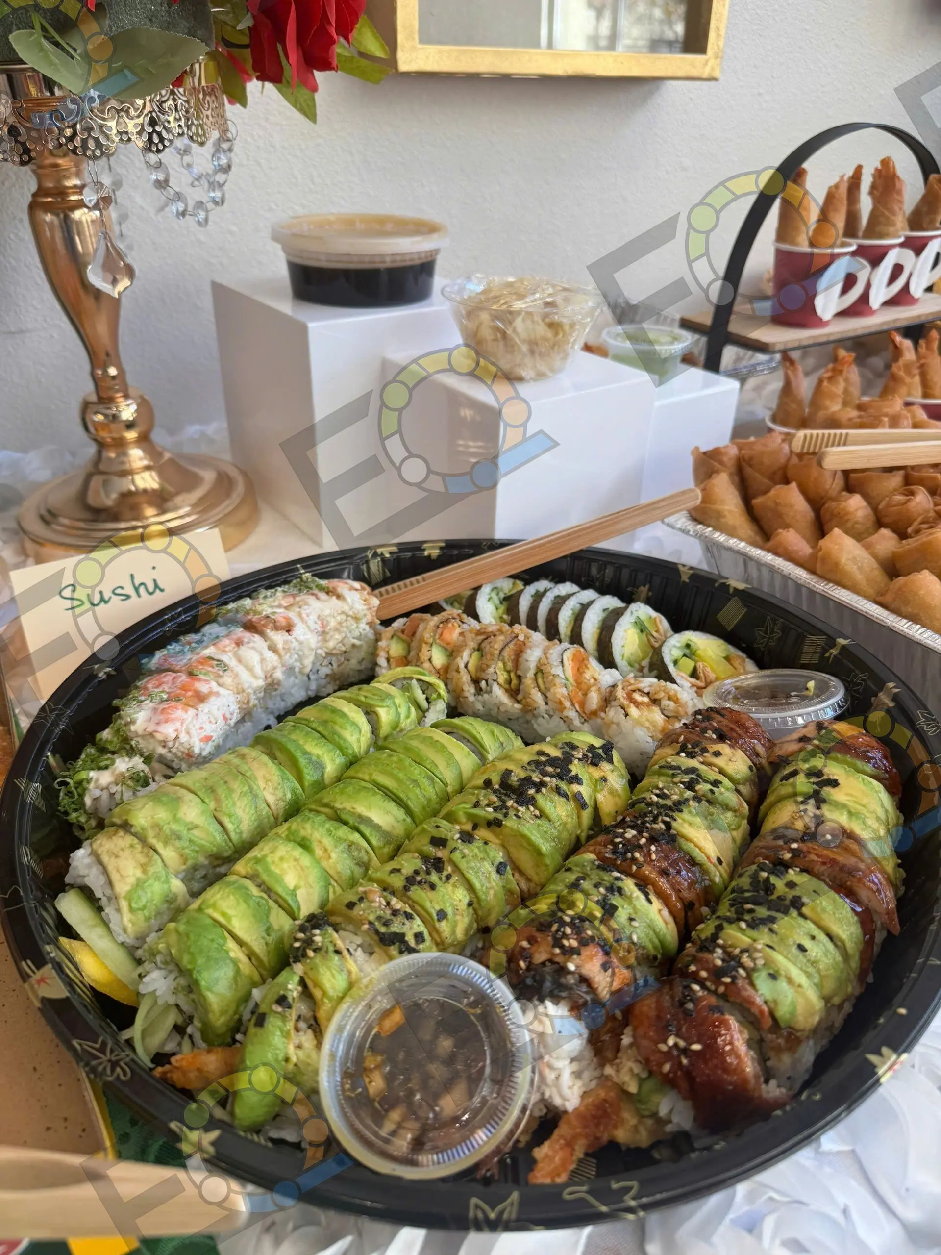 A black platter of sushi rolls with dipping sauce and a bread basket behind