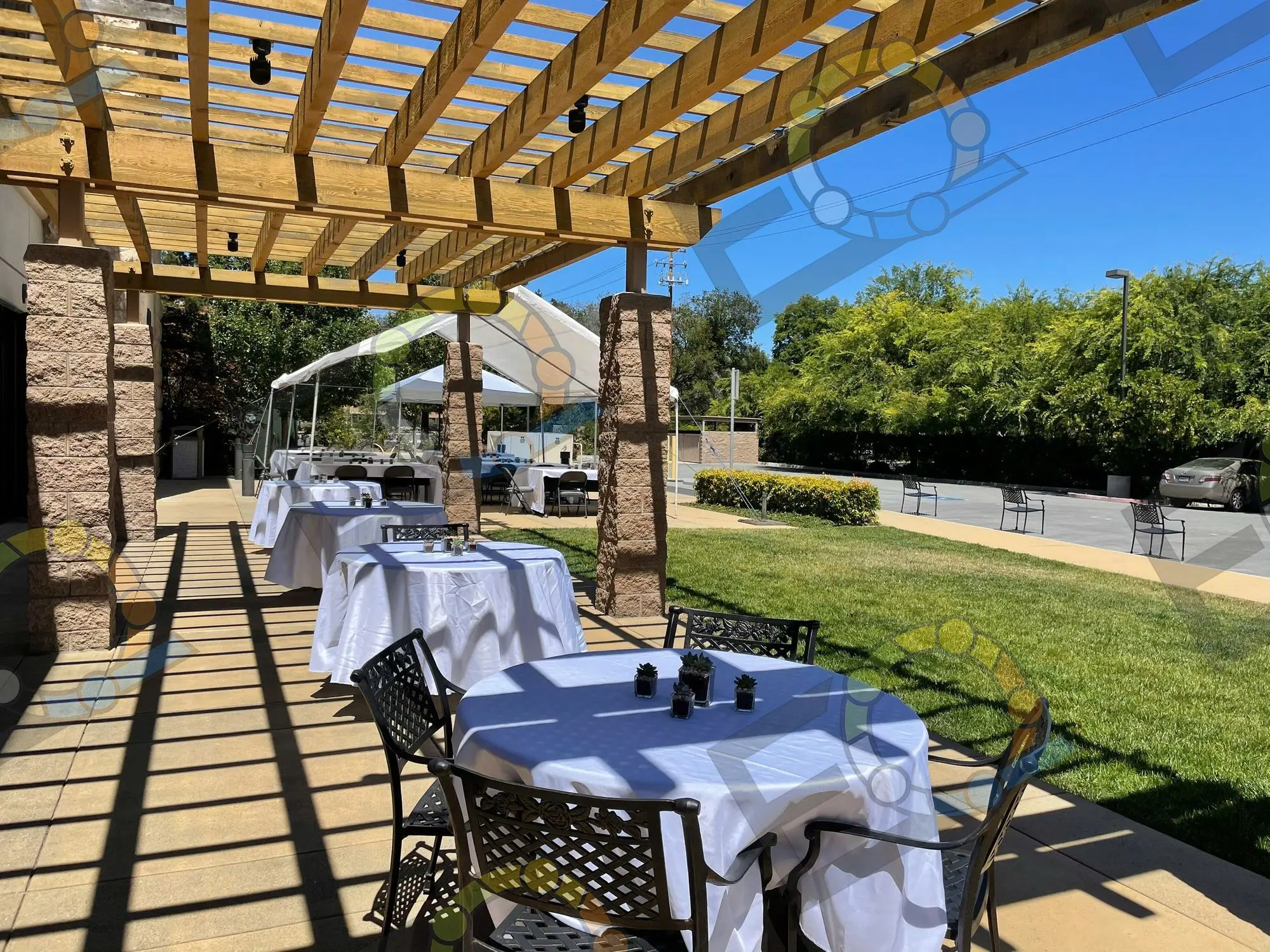 Patio tables in white linen under a pergola, set for an outdoor company event