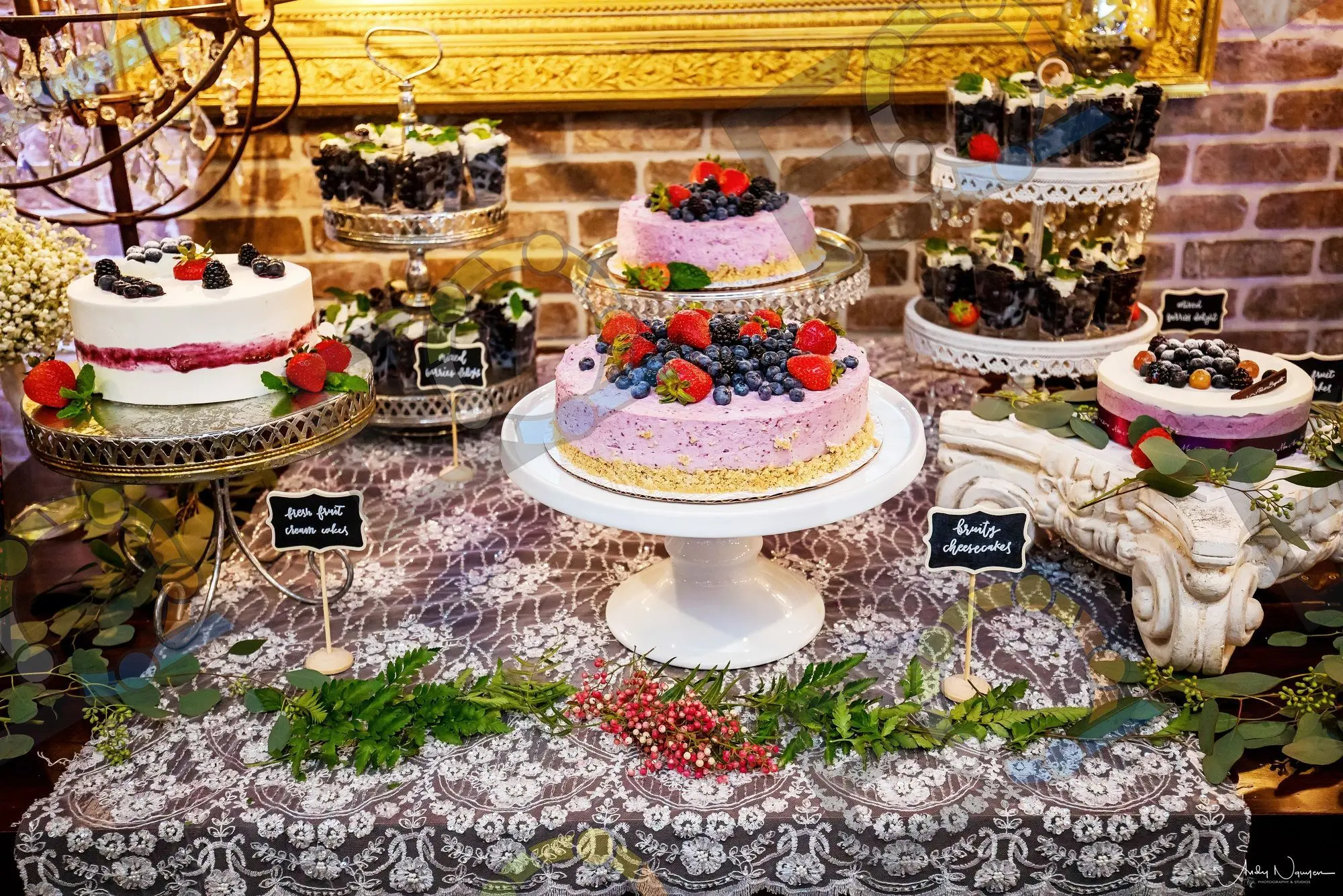 A dessert table of cakes and berry tarts on lace
