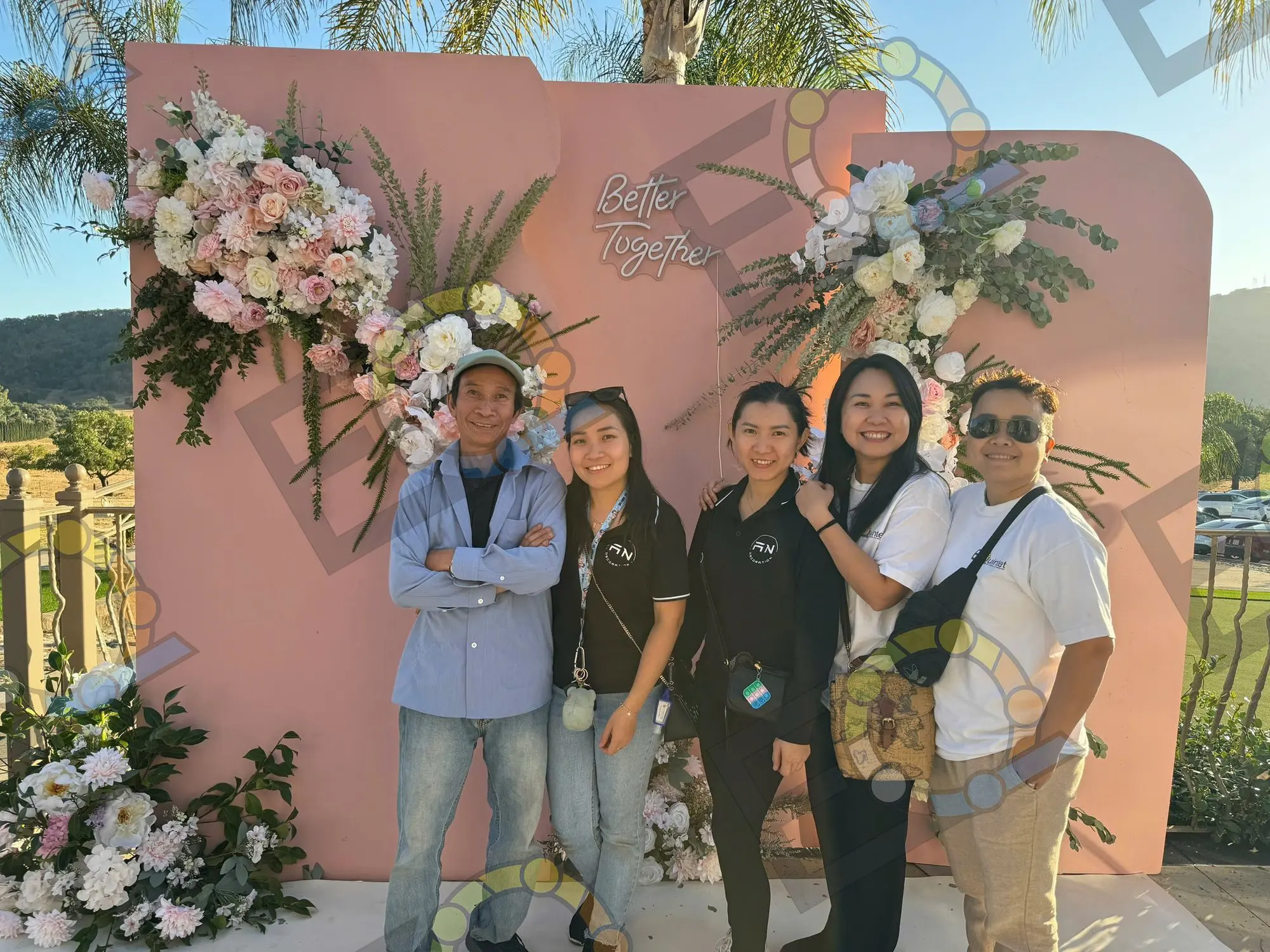 A group gathered at a blush floral backdrop reading Better Together