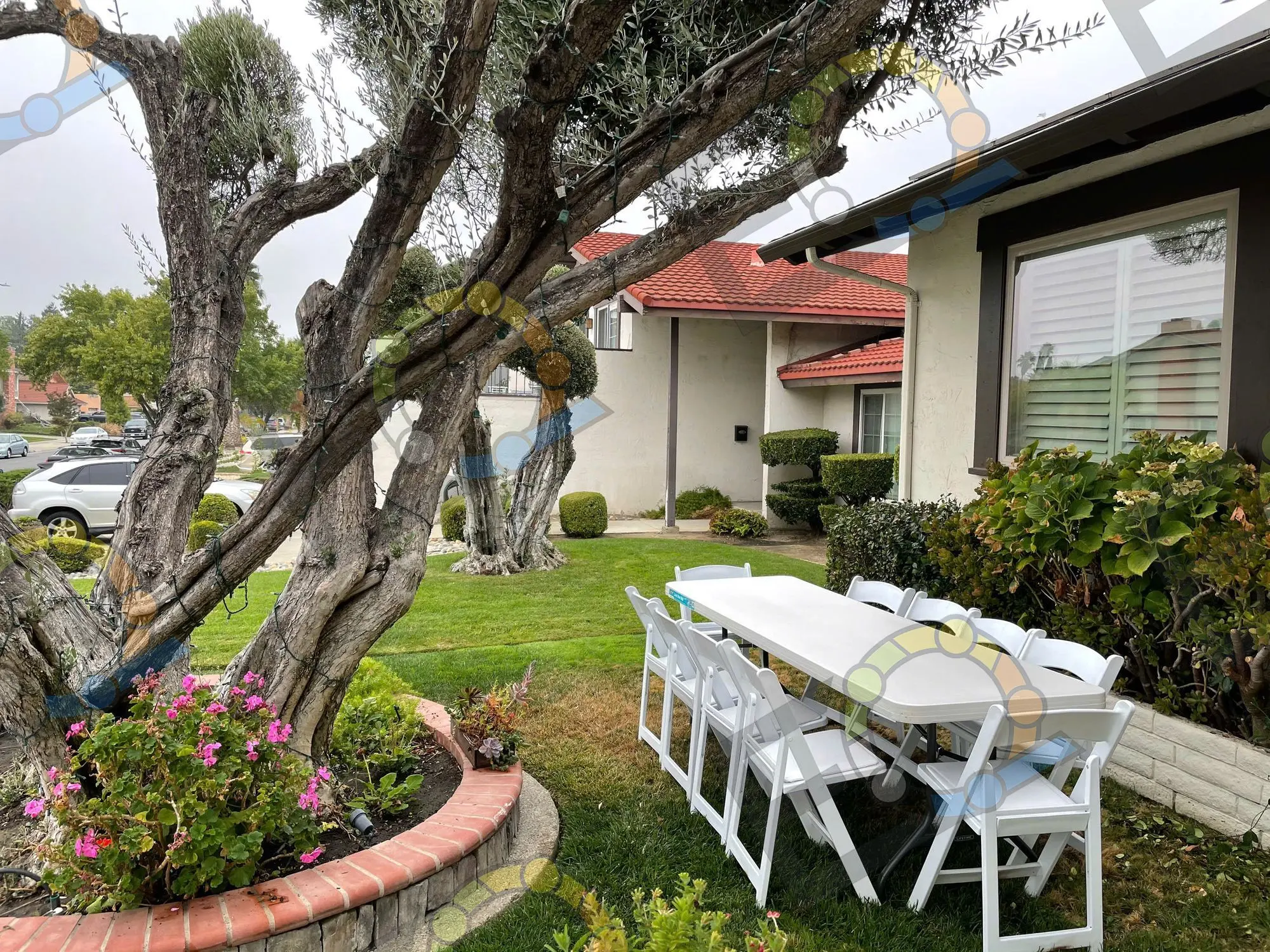 Folding tables and white chairs set for lunch beneath a garden tree