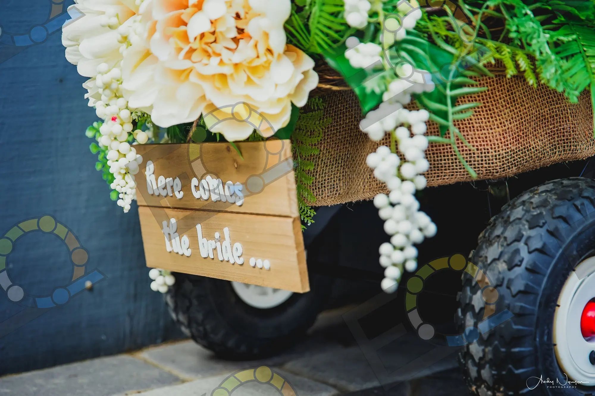 A hand-lettered Here Comes The Bride sign on a flower-trimmed wagon