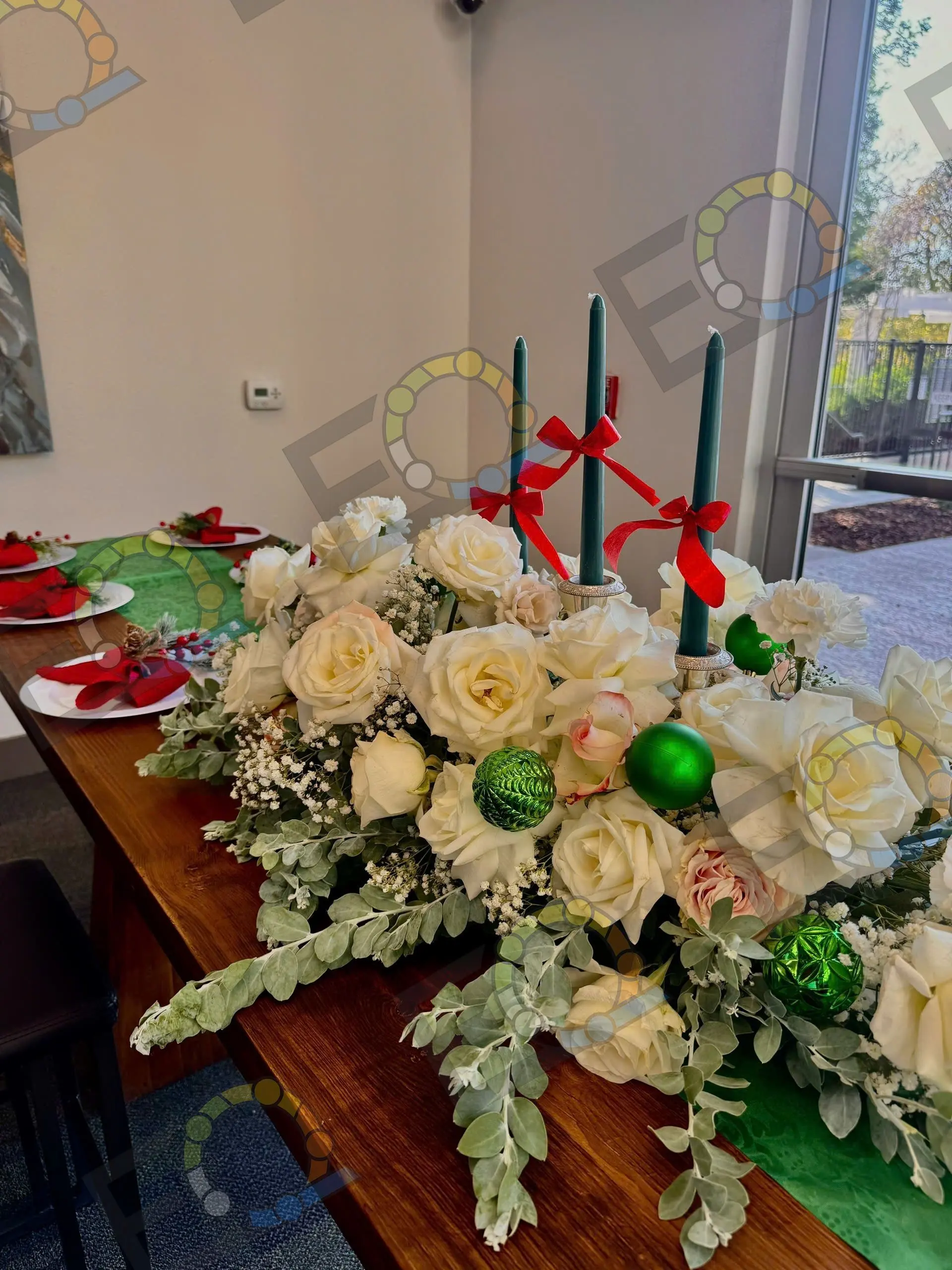 A white rose and dusty miller centrepiece with red candles on a wood table