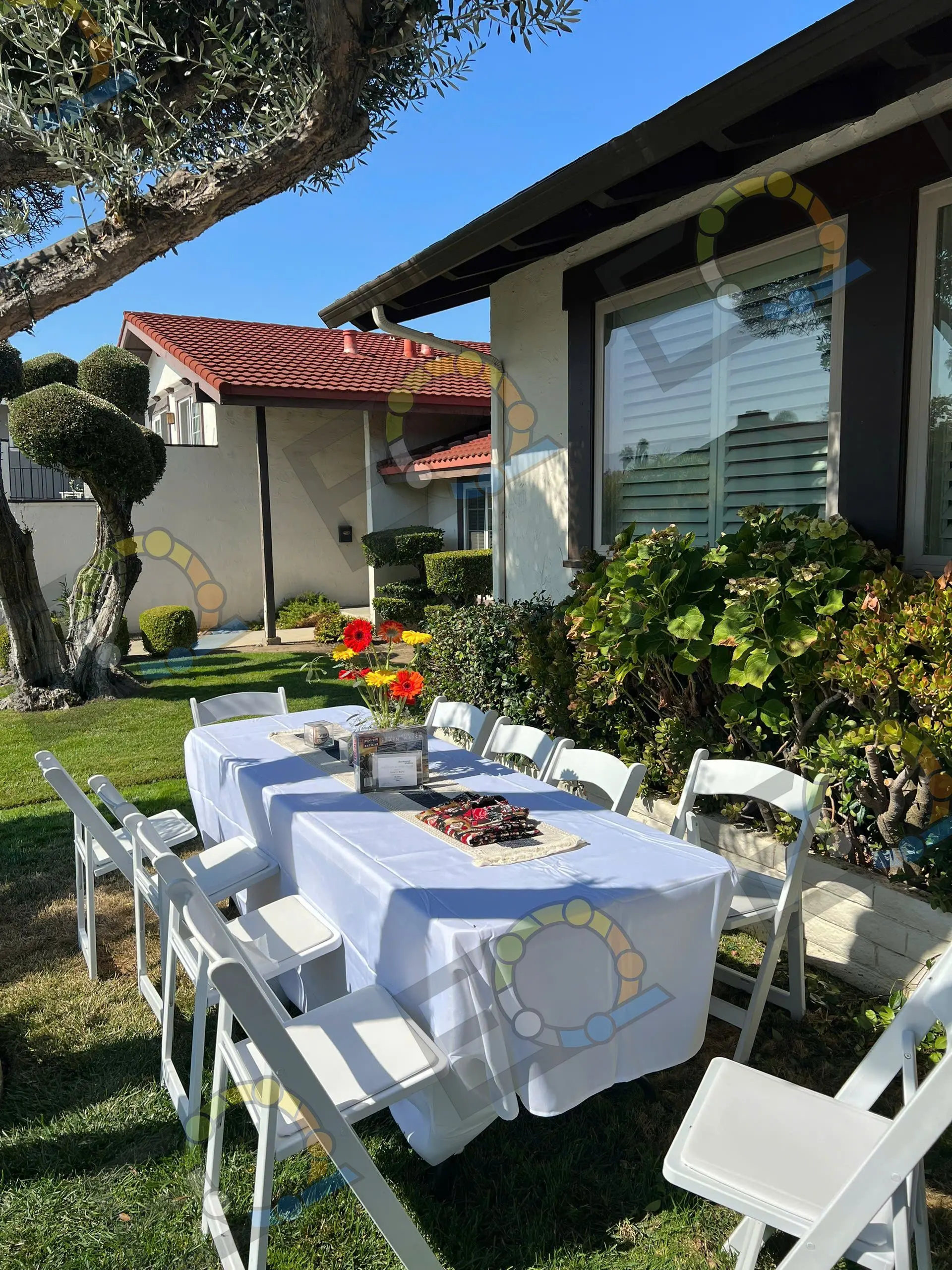 A long table laid with white linen beside a tiled-roof house